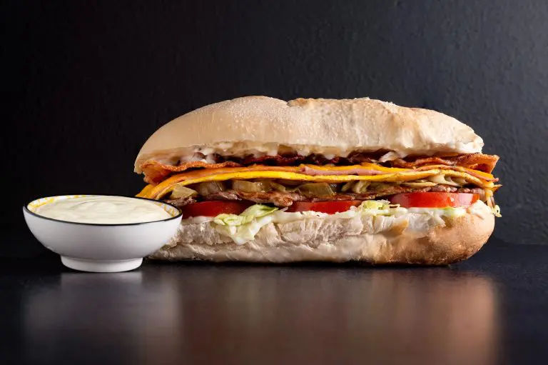 Primer plano de un auténtico lomito cordobés completo, mostrando su gran tamaño, pan suave especial, abundante mayonesa casera, carne tierna, huevo frito, jamón, queso, lechuga y tomate. Se diferencia visiblemente de un sándwich de lomo estándar por sus ingredientes y proporciones.