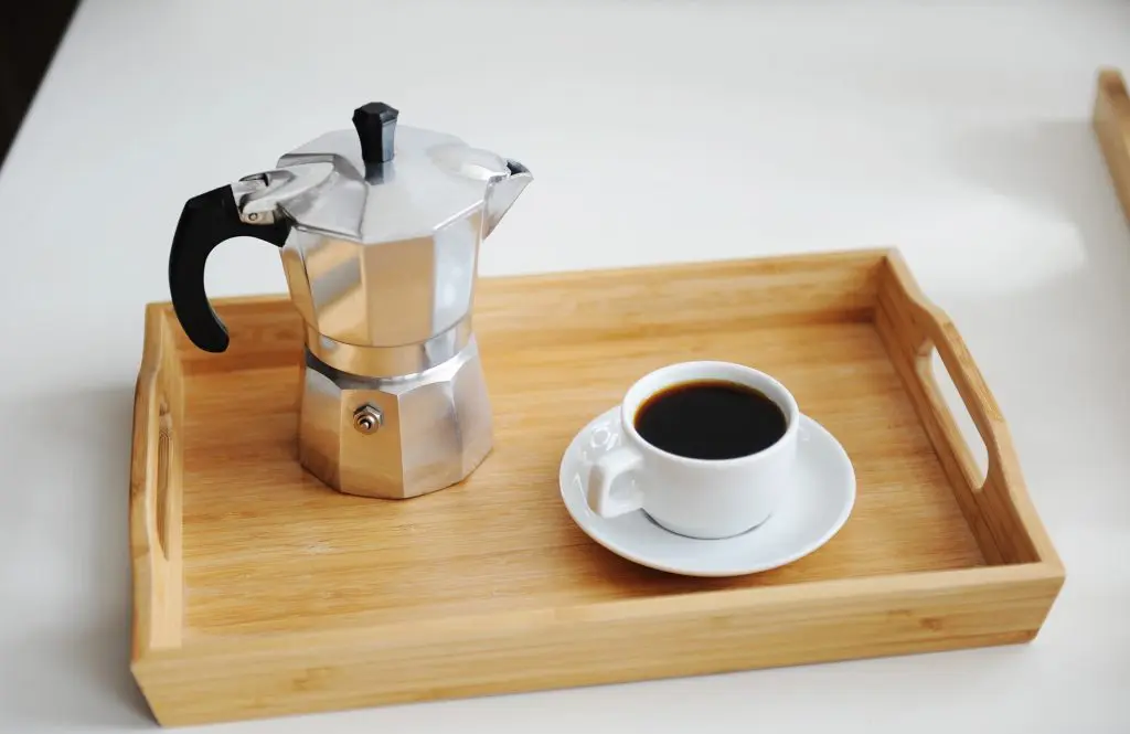Cafetera moka de aluminio junto a una taza de café sobre una bandeja de madera