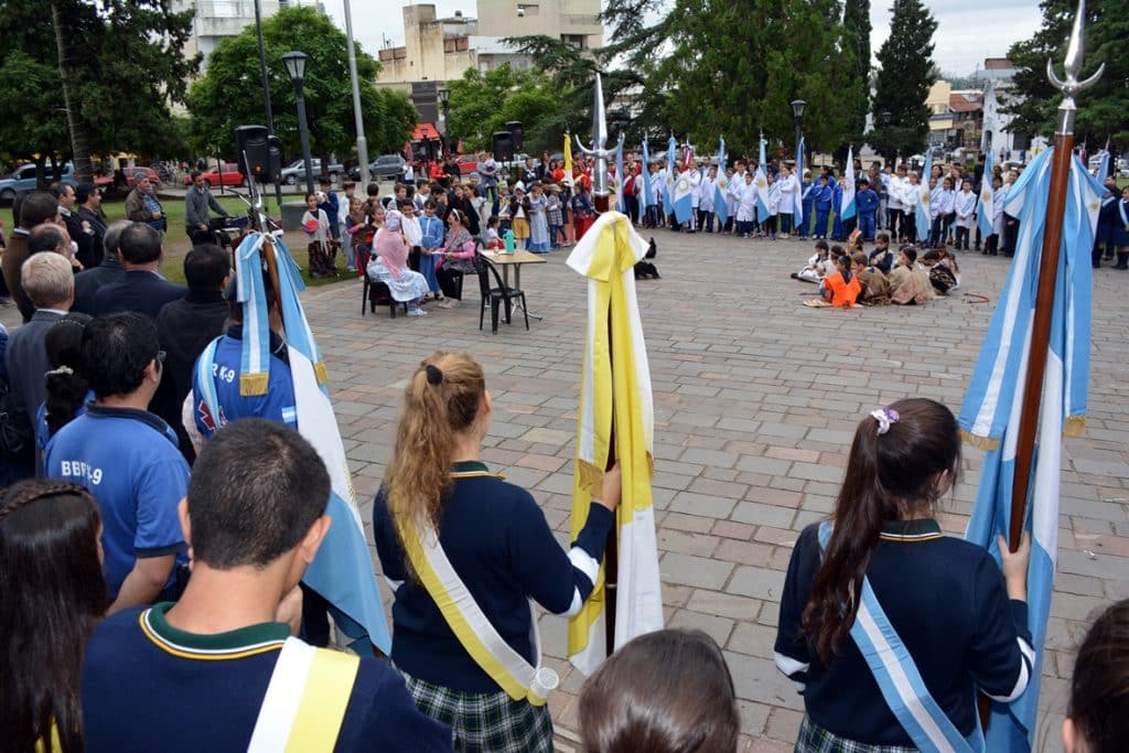 Un grupo de personas sosteniendo banderas en la plaza de Alta Gracia durante un acto.
